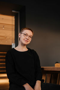 Young woman with short hair in eyeglasses and black sweater sitting at the table in office