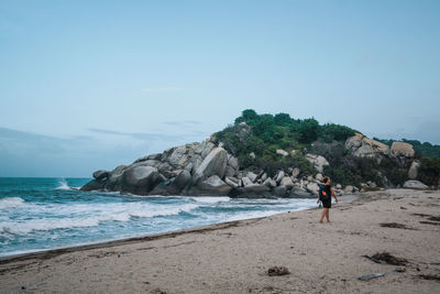 Rear view of woman walking at beach against sky