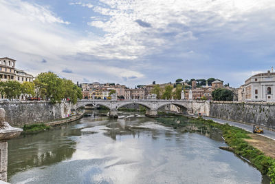 Bridge over river by buildings against sky