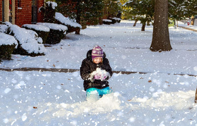 Girl kneeling while playing on snow against trees