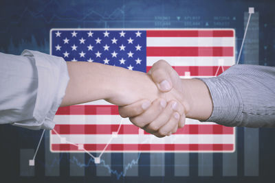 Cropped image of people shaking hands against american flag