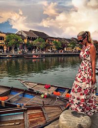 Woman standing by canal in city during sunset