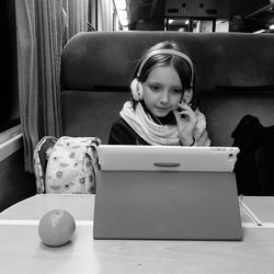 Girl using headphones while watching digital tablet on table in train