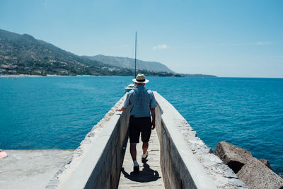 Rear view of man standing on sea against sky