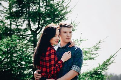 Young couple looking away while standing in forest during sunny day