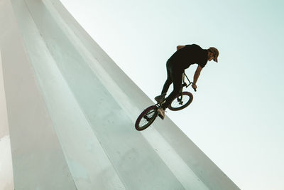 Man riding bicycle on built structure against sky