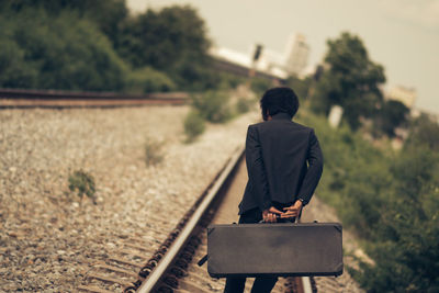 Businessman with suitcase walking on railroad track