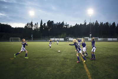 Girls running on soccer field against sky