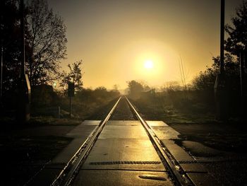 Railroad tracks amidst trees against sky during sunset