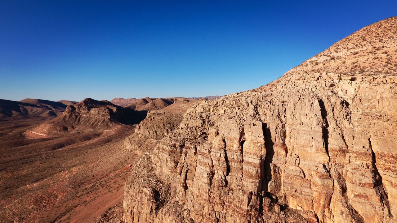 clear sky, blue, tranquility, tranquil scene, copy space, scenics, rock formation, landscape, beauty in nature, arid climate, nature, desert, physical geography, geology, barren, sunlight, sand, non-urban scene, mountain, rock - object