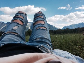 Midsection of person relaxing on field against sky