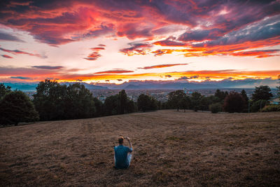 Rear view of men sitting on field against sky during sunset