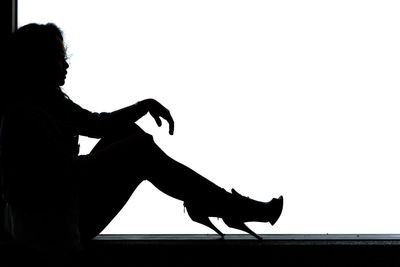 Side view of silhouette woman sitting on seat against clear sky