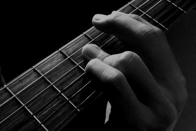 Close-up of hands playing guitar against black background