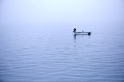 Man standing on moored fishing boat on calm lake during foggy weather