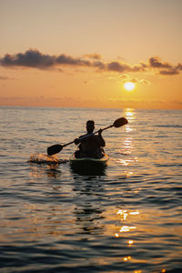 Silhouette man rowing on sea against sky during sunset