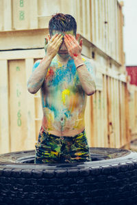 Shirtless young man with paint on body standing in tire