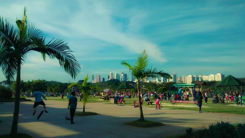 People on palm trees in city against sky