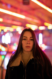 Portrait of young woman standing against illuminated light at night