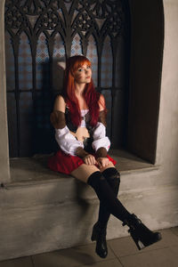 Portrait of fashion model wearing costume sitting on window sill