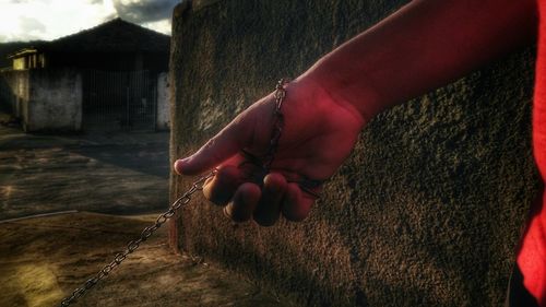 Cropped image of man holding chain by wall