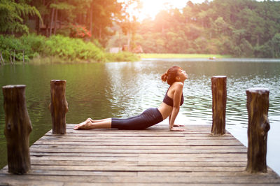 Rear view of woman sitting on pier over lake