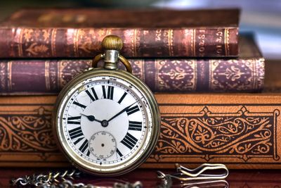 Close-up of pocket watch with stacked books on table