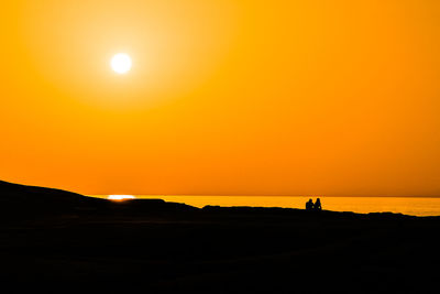 Silhouette people on land against sky during sunset