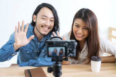 Smiling people waving at camera while sitting by table