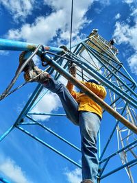 Low angle view of man climbing on rope against sky