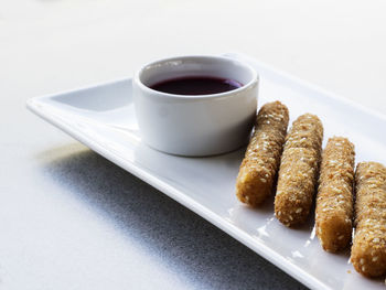 High angle view of fresh fried cheese with sauce in bowl on white plate