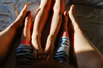 Close up view of mother, elder child and smaller child feet in the parent's bed under blanket