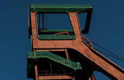 Low angle view of old machinery against clear blue sky