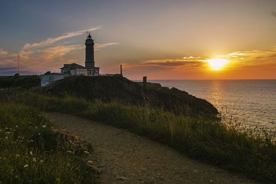 Lighthouse by sea against sky during sunset