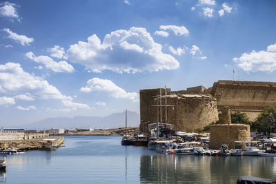 Sailboats moored on sea by buildings against sky