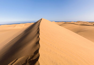 Sand dunes in desert against clear sky