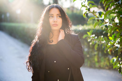 Portrait of beautiful young woman standing against trees