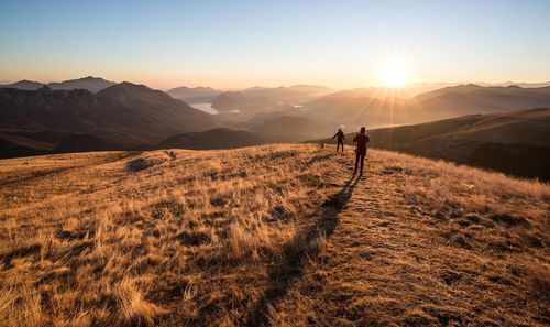 Women on field by mountains during sunrise