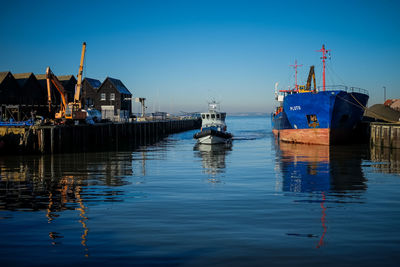 Fishing boats moored at harbor against clear blue sky