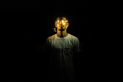 Man standing with illuminated string lights against black background
