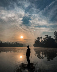 Silhouette man standing by lake against sky during sunset