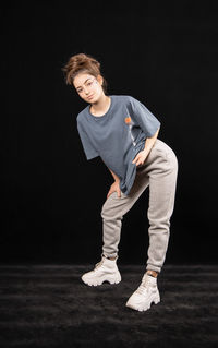 Portrait of teenage girl standing against black background