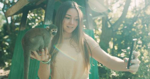 Portrait of smiling young woman holding plant against trees