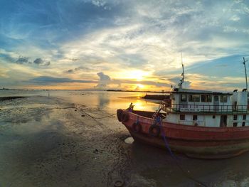 Boat moored on shore at beach against sky during sunset