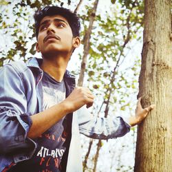 Low angle view of young man standing by tree trunk