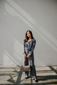 Portrait of young woman standing against wall