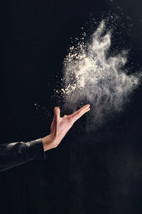 Close-up of hand throwing talcum powder against black background