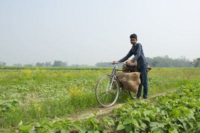 Young farmer riding bicycle carrying vegetable bag after harvest