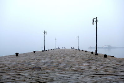 Street lights on pier by sea against clear sky