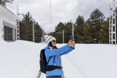 Woman photographing while standing on snow covered landscape